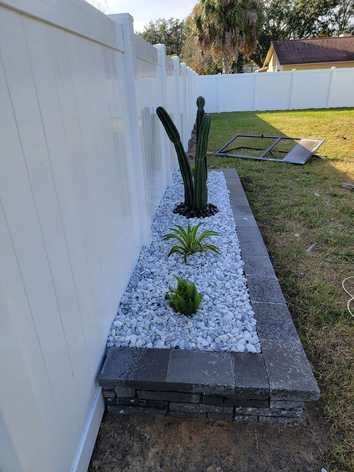 Rock garden bed with cactus and agave installed along a fence line
